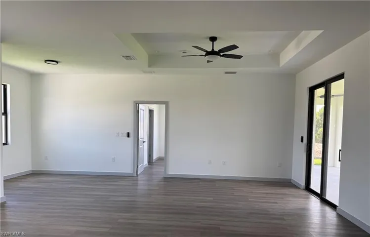 Spacious interior featuring wood-finish flooring, a tray ceiling with a ceiling fan, and white walls