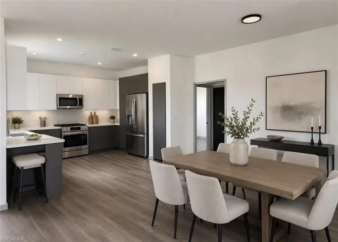Contemporary kitchen and dining area featuring stainless steel appliances, two-tone cabinetry, recessed lighting, and wood-finish flooring