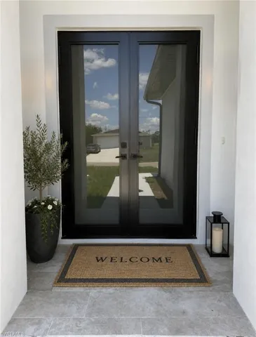 Double-door entry featuring dark frames and full-light glass panels, tiled entryway-Virtually Staged