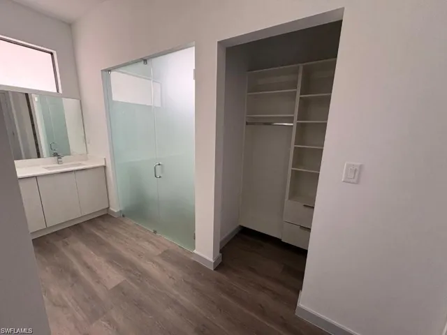 Contemporary bathroom featuring a frosted glass shower enclosure, single vanity with a white countertop, and wood-finish flooring