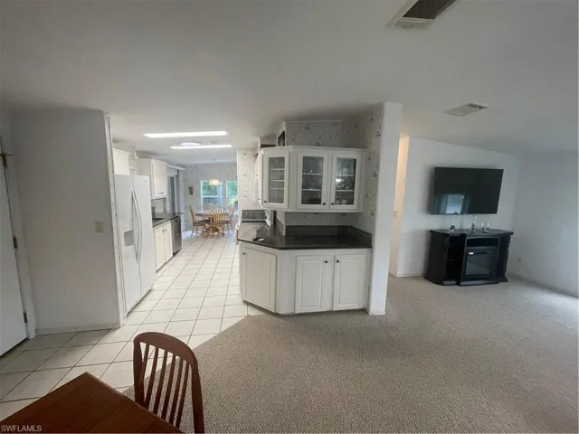 Kitchen with white cabinets, glass insert cabinets, light tile patterned floors, fridge, and light carpet
