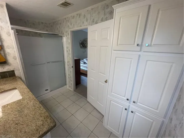 Ensuite bathroom featuring wallpapered walls, a shower stall, light tile patterned floors, and vanity