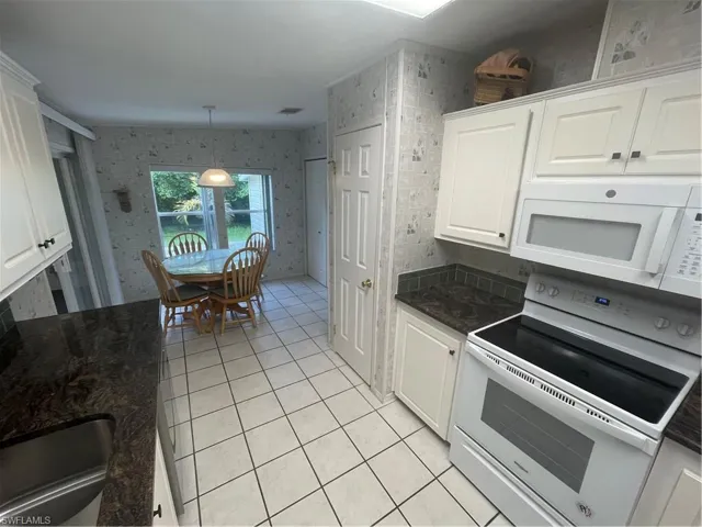 Kitchen with stove, wallpapered walls, dark stone counters, and white cabinets