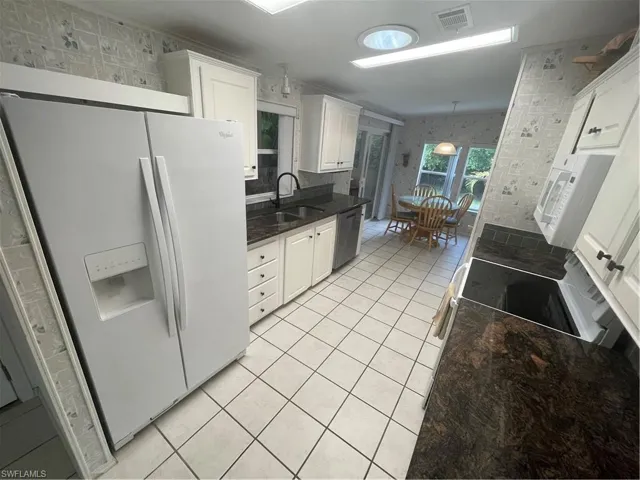 Kitchen with wallpapered walls, refrigerator, white cabinetry, light tile patterned floors, and stainless steel range oven