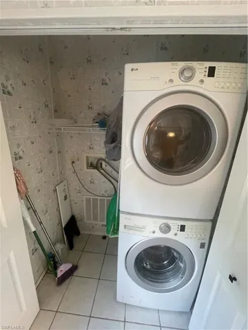 Washroom featuring light tile patterned floors, tile walls, and stacked washing machine and dryer