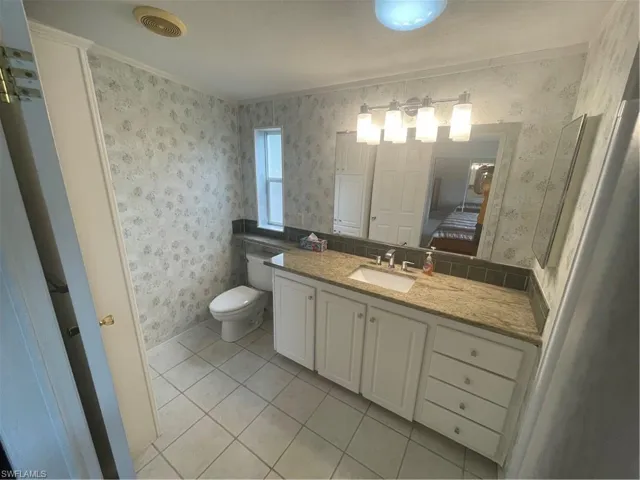 Bathroom featuring light tile patterned floors, vanity, wallpapered walls, connected bathroom, and crown molding
