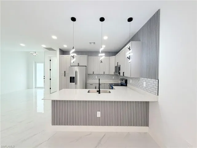 Kitchen with white cabinetry, stainless steel appliances, a subway tile backsplash, and a breakfast bar with pendant lighting