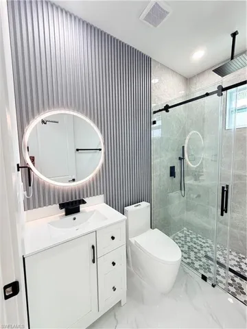 White vanity with integrated sink, backlit circular mirror, and matte black fixtures