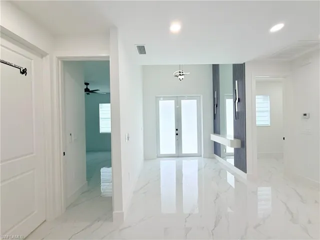 White marble-look flooring, recessed lighting, white double-panel doors, and a decorative wall feature with integrated lighting