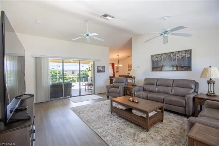 Living area with vaulted ceiling, ceiling fan with notable chandelier, light wood-style flooring, and visible vents