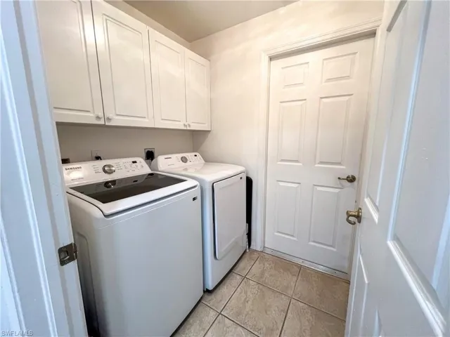 Laundry room with cabinet space, light tile patterned flooring, and washing machine and clothes dryer