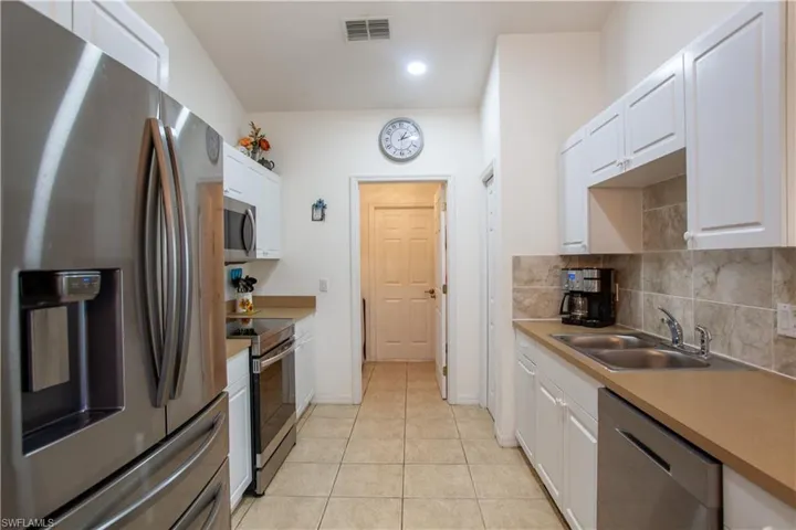 Kitchen featuring visible vents, decorative backsplash, white cabinets, a sink, and appliances with stainless steel finishes