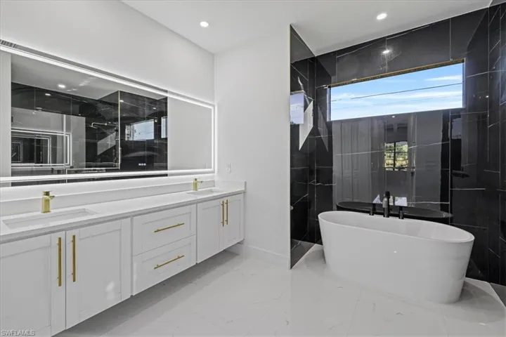 Full bathroom with double vanity, a freestanding bath, walk in shower, recessed lighting, and light marble finish flooring