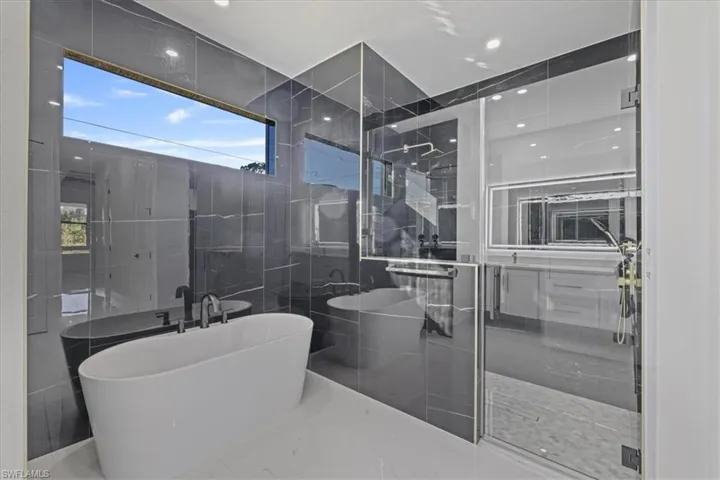 Bathroom with a shower stall, a freestanding tub, tile walls, and recessed lighting