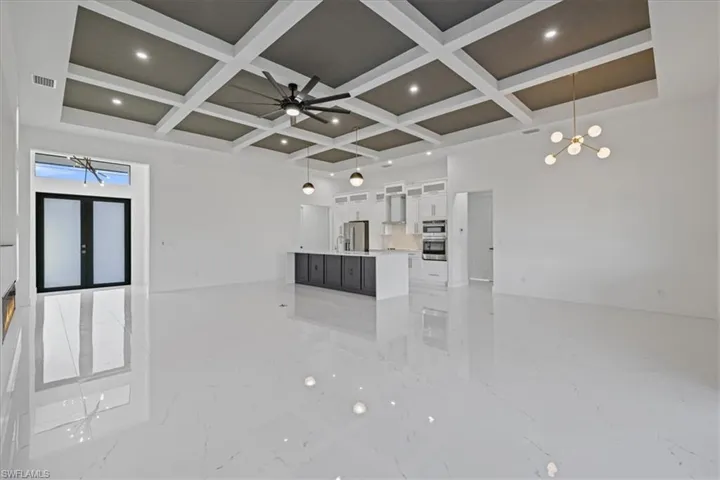 Unfurnished living room with coffered ceiling, light marble finish floors, ceiling fan, a chandelier, and french doors