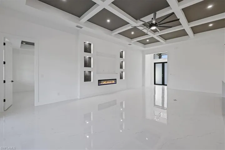 Empty room with coffered ceiling, a glass covered fireplace, recessed lighting, ceiling fan, and light marble finish flooring