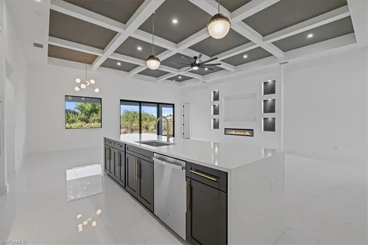 Kitchen featuring light stone countertops, dishwasher, a glass covered fireplace, coffered ceiling, and light marble finish flooring