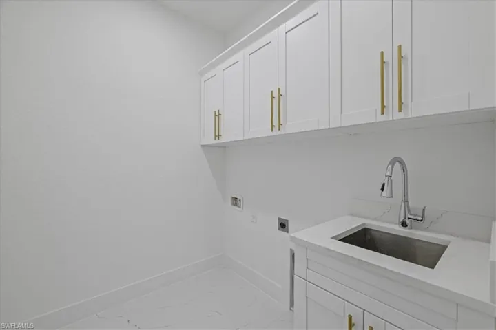 Laundry area with electric dryer hookup, cabinet space, hookup for a washing machine, and light marble finish flooring