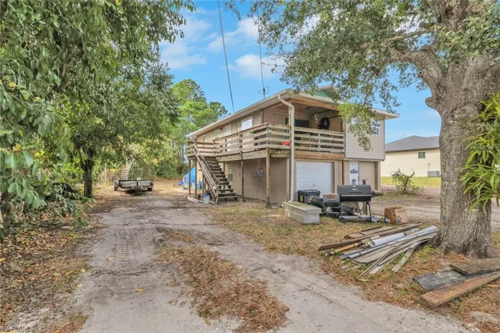 Back of property with stairway, dirt driveway, a wooden deck, and an attached garage