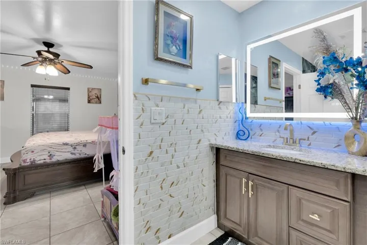 Ensuite bathroom featuring vanity, tile walls, light tile patterned floors, ceiling fan, and wainscoting