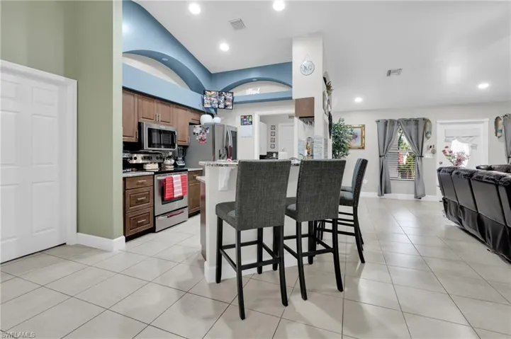 Kitchen with stainless steel appliances, a kitchen bar, light tile patterned flooring, open floor plan, and recessed lighting