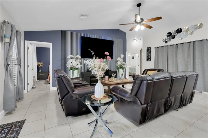 Living room featuring lofted ceiling, light tile patterned floors, a ceiling fan, and an accent wall