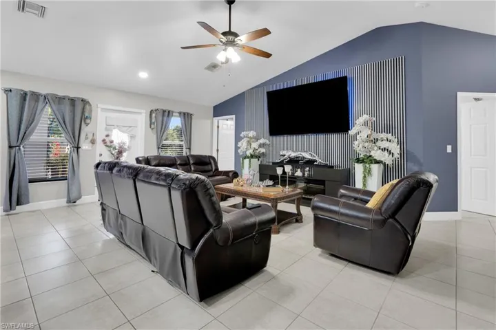 Living area featuring an accent wall, vaulted ceiling, light tile patterned floors, and ceiling fan