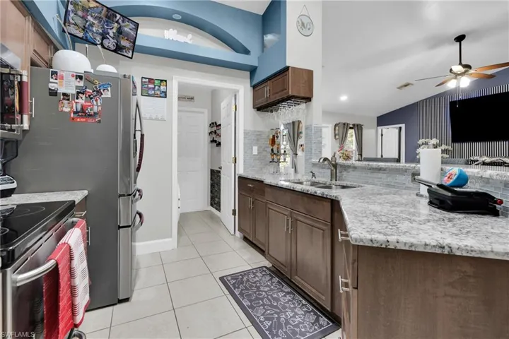 Kitchen featuring light tile patterned flooring, light stone counters, stainless steel appliances, a ceiling fan, and lofted ceiling