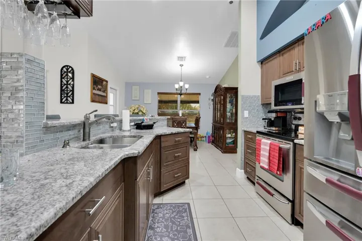 Kitchen featuring tasteful backsplash, stainless steel appliances, light tile patterned floors, light stone counters, and a peninsula