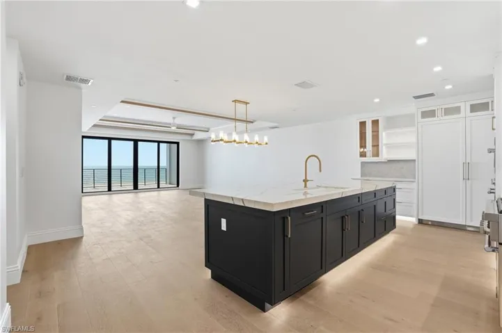 Dual tone kitchen featuring glass fronted cabinets, dual tone cabinets, an island with sink, light stone counters, and open floor plan