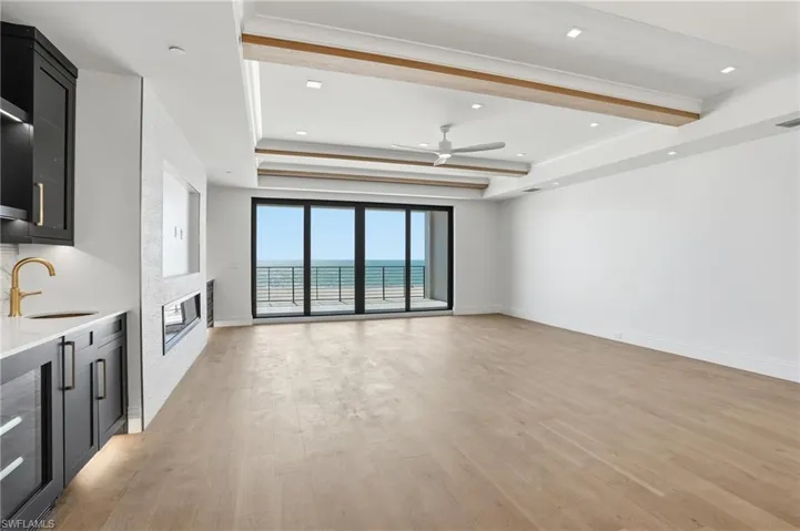 Unfurnished living room with light wood-style floors, a ceiling fan, beverage cooler, a glass covered fireplace, and a tray ceiling