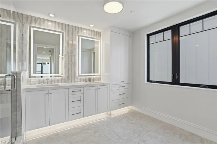 Full bath featuring double vanity, a shower stall, and light marble finish flooring