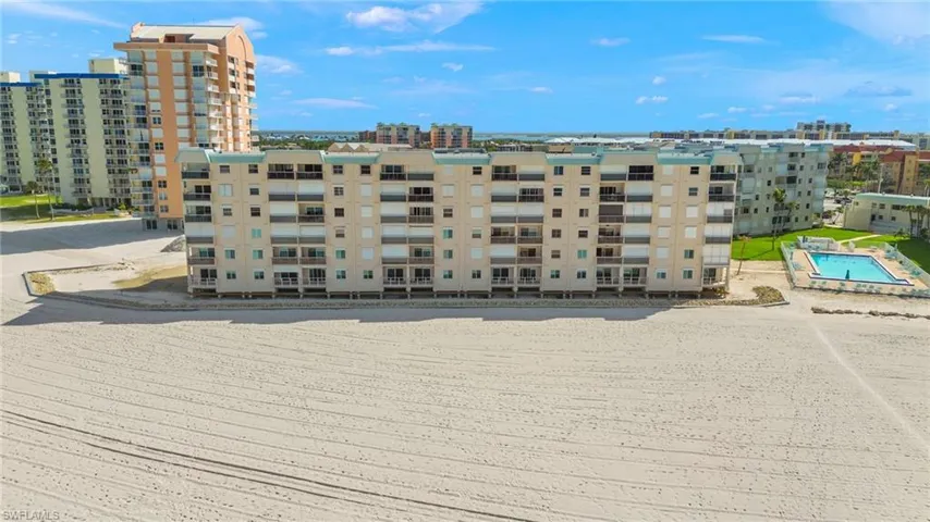 Multi-story residential building featuring private balconies overlooking a sandy beachfront
