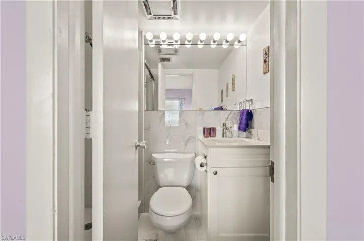 Compact bathroom featuring a white vanity with a light-toned countertop, a large mirror with integrated lighting, and white tile wainscoting