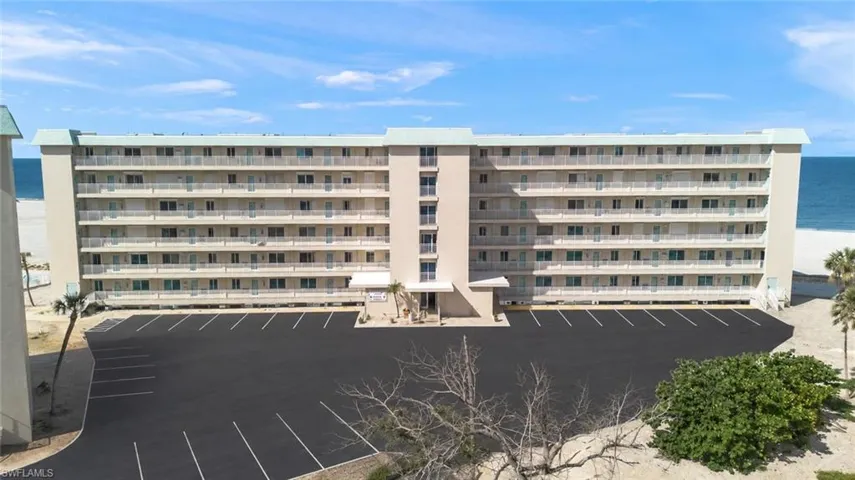 Beachfront multi-story building featuring multiple private balconies, a large parking area, and direct beach access