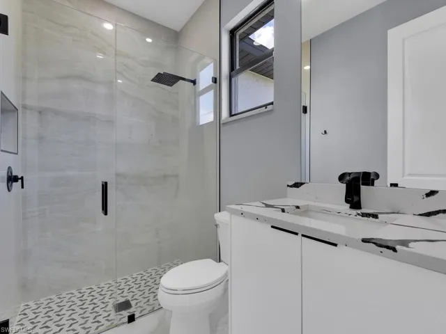 Bathroom featuring a shower with door, vanity, and toilet
