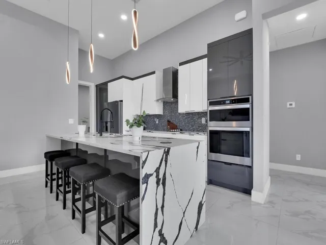 Kitchen with hanging light fixtures, light tile floors, wall chimney range hood, sink, and appliances with stainless steel finishes