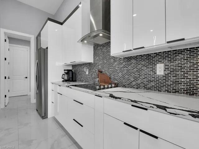 Kitchen with stainless steel refrigerator, white cabinets, wall chimney exhaust hood, and light tile flooring
