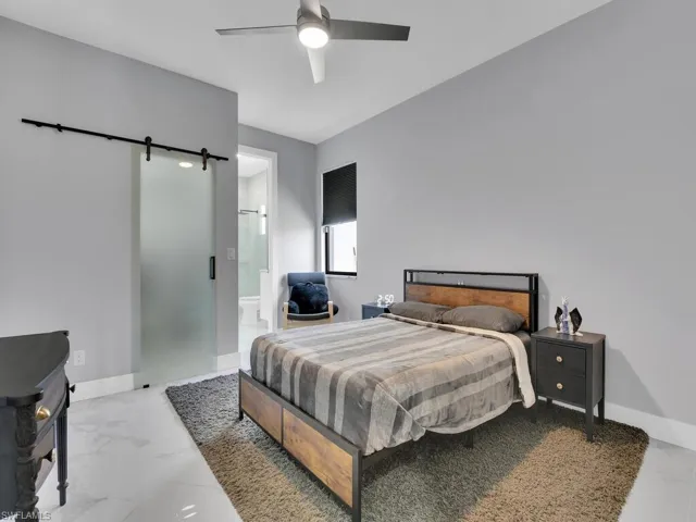 Bedroom with a barn door, ceiling fan, and ensuite bath