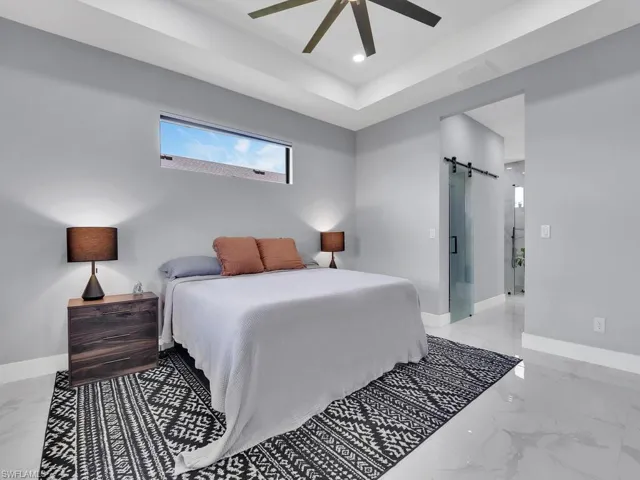 Bedroom with a barn door, light tile flooring, ceiling fan, and a raised ceiling