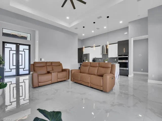 Living room with a high ceiling, light tile flooring, ceiling fan, and a raised ceiling