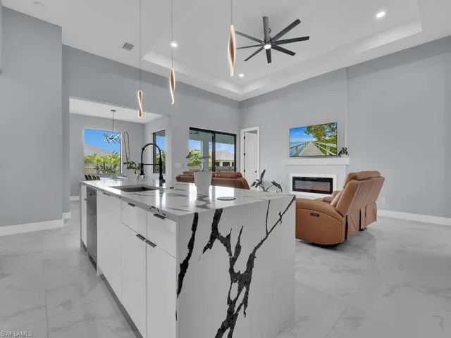 Kitchen featuring decorative light fixtures, light tile flooring, a center island with sink, a raised ceiling, and white cabinetry