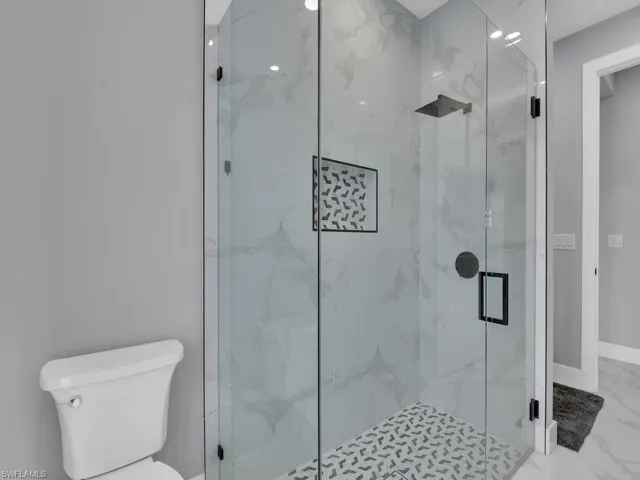 Bathroom featuring a shower with door, tile flooring, and toilet