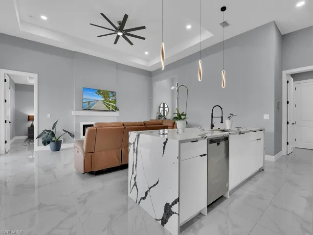 Kitchen featuring white cabinetry, a center island with sink, decorative light fixtures, ceiling fan, and a raised ceiling