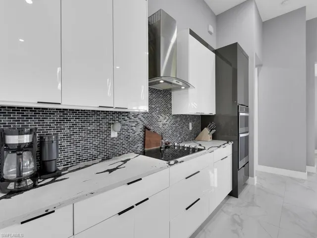 Kitchen with black gas cooktop, white cabinetry, light stone countertops, wall chimney exhaust hood, and light tile floors