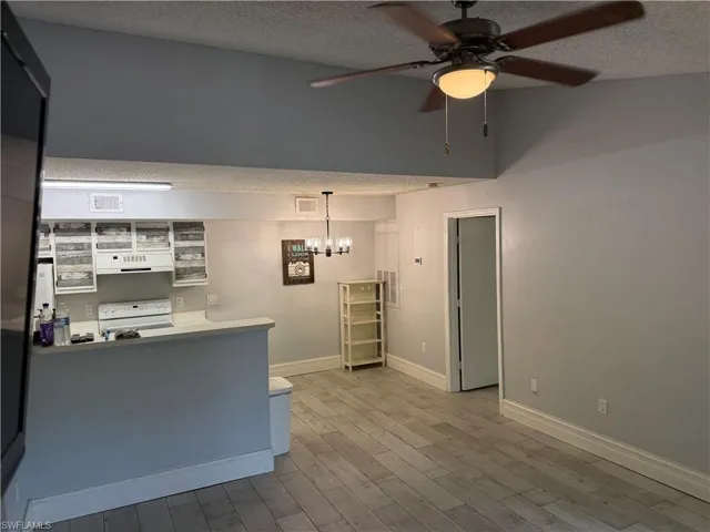 Open-concept living space featuring wood-finish flooring, a ceiling fan with integrated lighting, and a modern chandelier