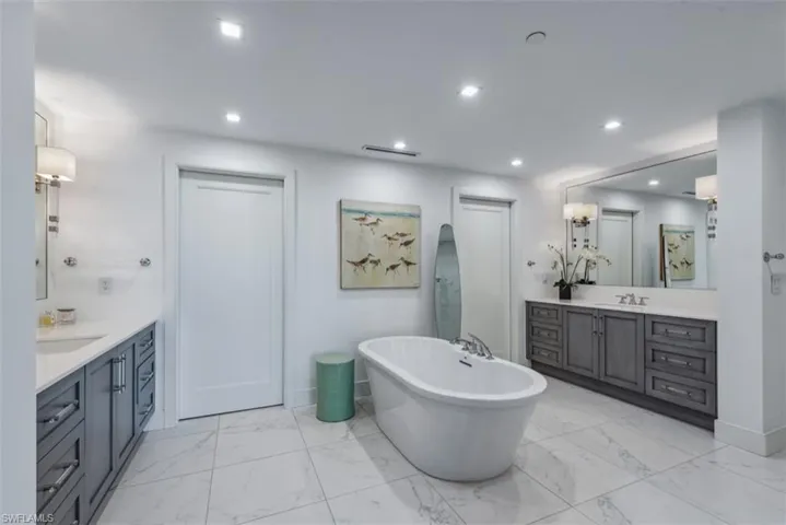 Bathroom with two vanities, a soaking tub, light marble finish floors, and recessed lighting