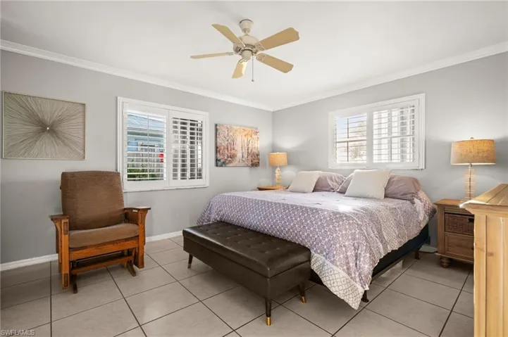 The primary bedroom showcases attractive plantation shutters, crown molding, multiple windows, a ceiling fan, and light tile patterned floors. No carpet here.