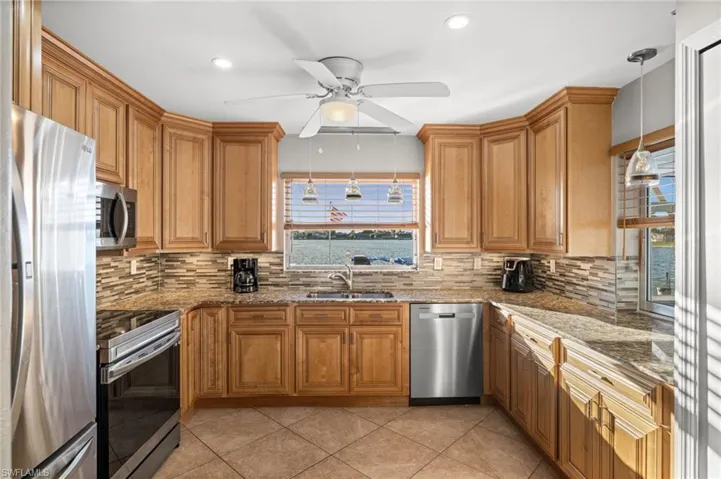 The beautifully renovated kitchen offers raised, ceiling height cabinetry, granite countertops, a beautiful backsplash, and soft close cabinets. Just look at that view!Kitchen featuring brown cabinets, appliances with stainless steel finishes, pendant lighting, and recessed lighting.
