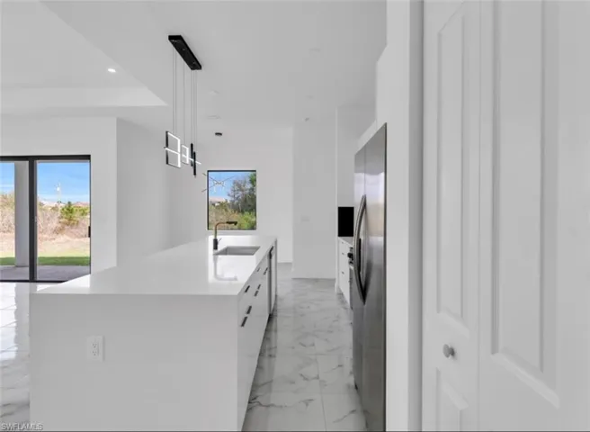 Kitchen with white cabinets, pendant lighting, freestanding refrigerator, a large island, and light stone countertops